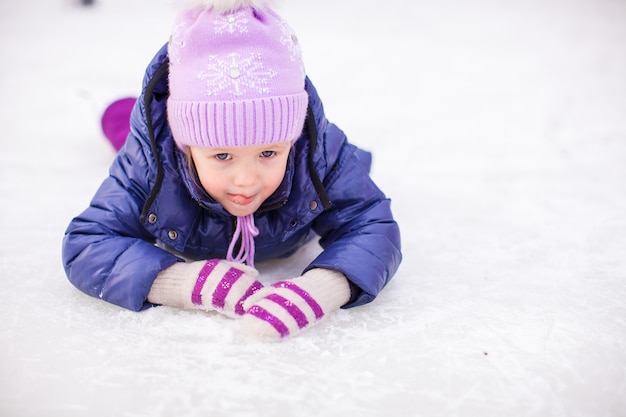 Bambina adorabile che si siede sul ghiaccio con i pattini dopo la caduta