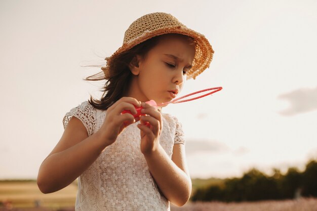 Bambina adorabile che soffia bolle di sapone fuori al parco giochi. Dolce bambino che gioca con le bolle fuori contro il tramonto.