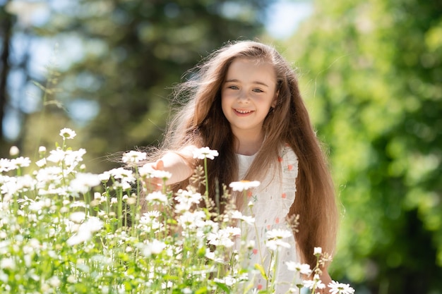 Bambina adorabile con bei capelli che giocano vicino ai fiori nell'estate del parco