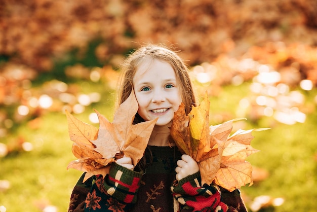 Bambina adorabile con foglie d'autunno nel parco di bellezza Bambina felice che ride e gioca a lea