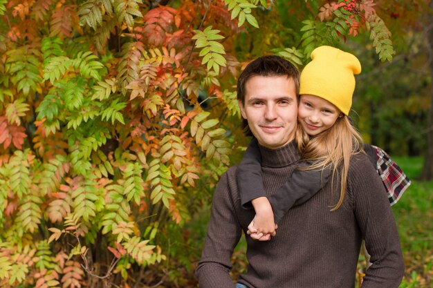 Bambina adorabile con il padre felice divertendosi nel parco di autunno un giorno soleggiato