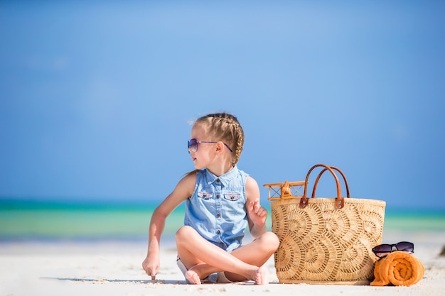 Bambina adorabile con la borsa e l'asciugamano di spiaggia sulla spiaggia bianca