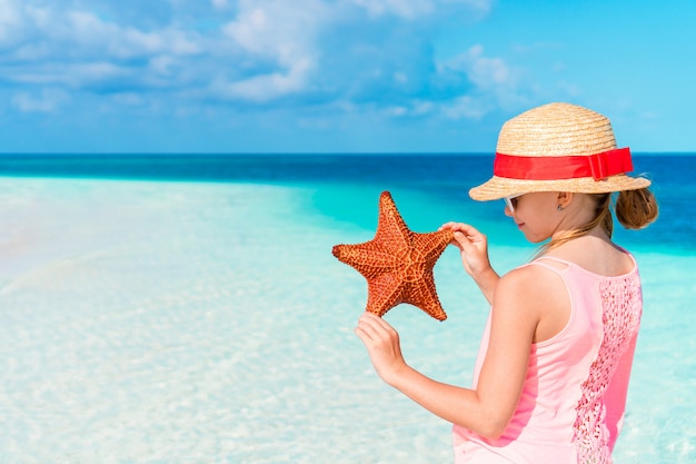 Bambina adorabile con le stelle marine sulla spiaggia vuota bianca