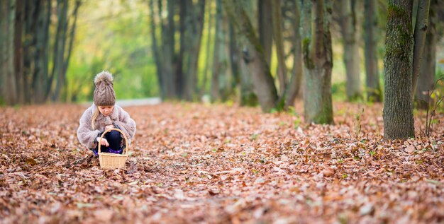 Bambina adorabile con un cestino nel giorno di autunno all'aperto in bella foresta