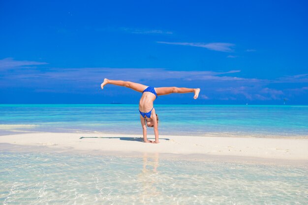 Bambina adorabile divertendosi facendo cartwheel sulla spiaggia sabbiosa bianca tropicale