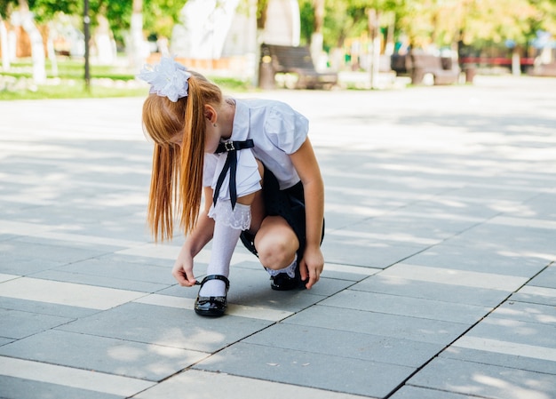 Bambina adorabile divertente nel parco o nel cortile della scuola. Il bambino regola la chiusura della scarpa.