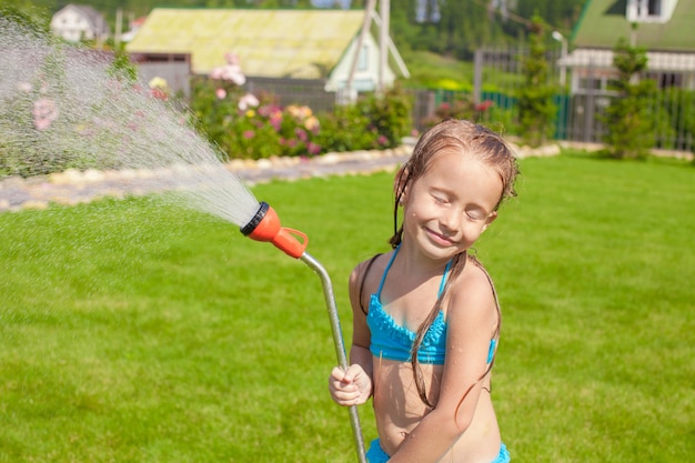 Bambina adorabile felice che sorride e che versa acqua da un tubo flessibile