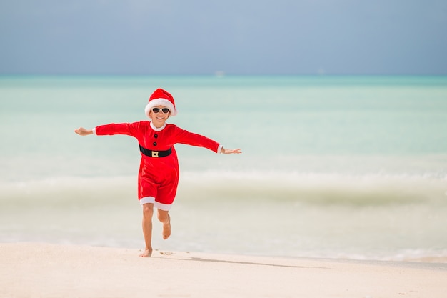 Bambina adorabile in cappello di Santa sulla spiaggia tropicale