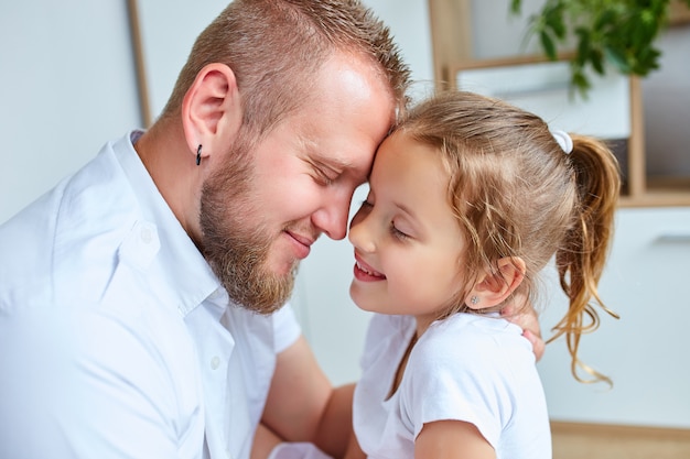 Bambina adorabile in vestito bianco che abbraccia padre amoroso