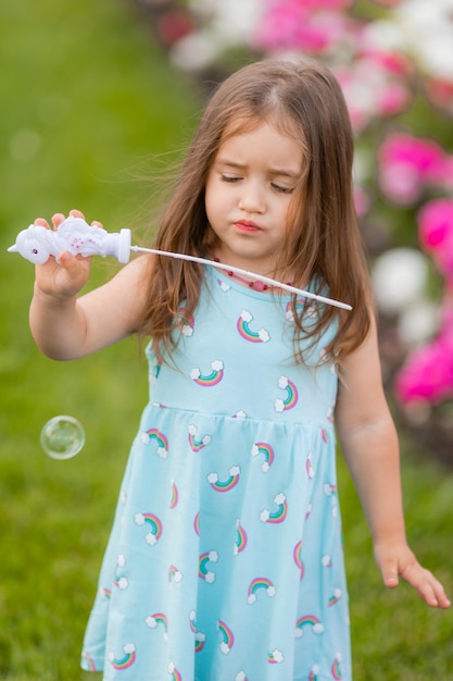 Bambina adorabile in vestito blu con bolle di sapone nell'estate del parco