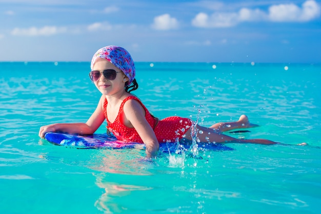 Bambina adorabile su una tavola da surf nel mare turchese