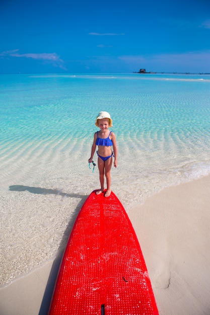 Bambina adorabile su una tavola da surf nel mare turchese