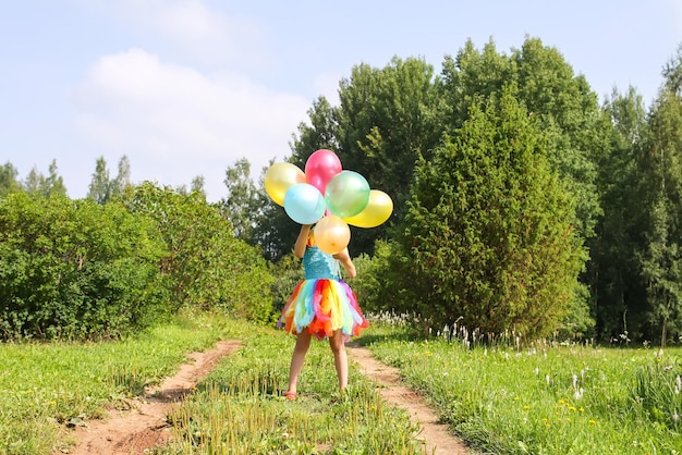 Bambina adorabile sull'erba verde in campagna con palloncini luminosi colorati