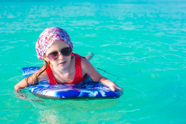 Bambina adorabile sulla tavola da surf nel mare turchese