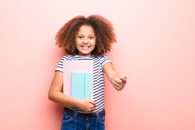 Bambina afroamericana contro la parete piana che tiene un libro