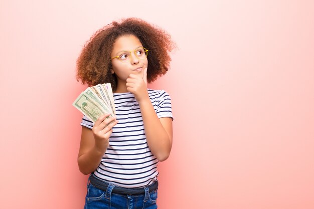 Bambina afroamericana contro la parete piana con le banconote del dollaro