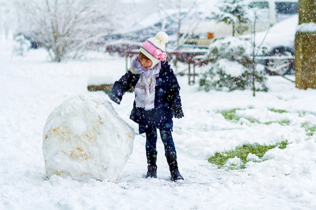 Bambina all'aperto in inverno vicino a una grande palla di neve