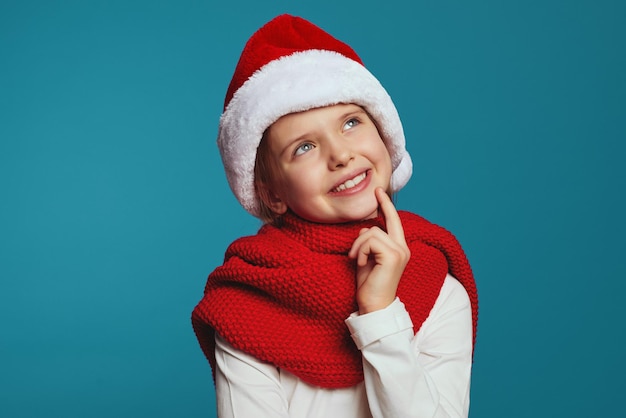Bambina allegra che indossa cappello di Natale e sciarpa rossa che guarda l'obbiettivo