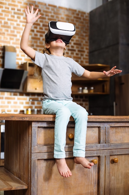 Bambina allegra che indossa gli occhiali VR mentre era seduto in cucina