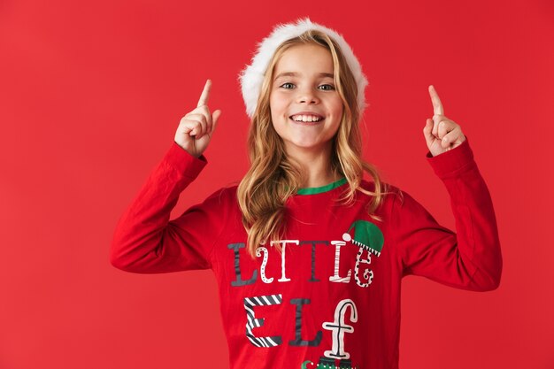 Bambina allegra che indossa il costume di Natale in piedi isolato, rivolto verso l'alto