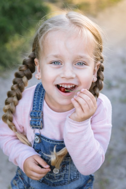 Bambina allegra che mangia le ciliege nel giardino di estate. Un bambino mangia le bacche in giardino.