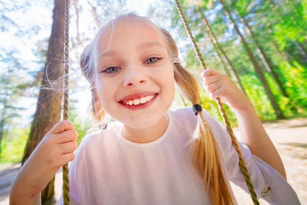 Bambina allegra che oscilla su un'altalena all'aperto nella foresta Primo piano