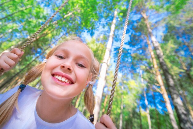 Bambina allegra che oscilla su un'altalena all'aperto nella foresta Primo piano