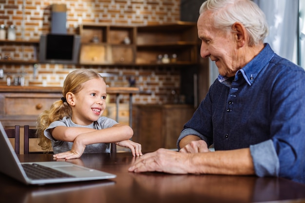 Bambina allegra che sorride mentre parla con suo nonno in cucina