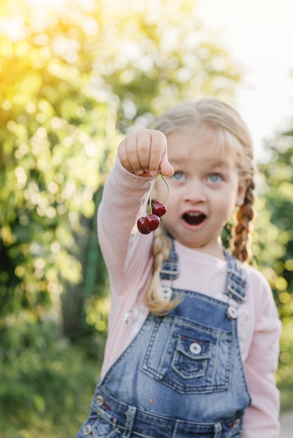 Bambina allegra che tiene le ciliegie in giardino d'estate