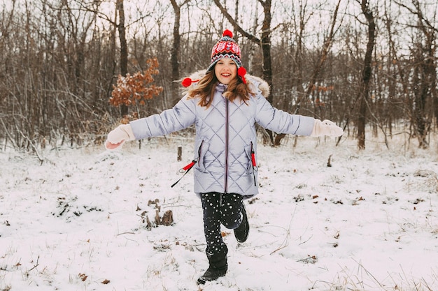 Bambina allegra felice che si diverte nella foresta in una giornata invernale. il bambino gioca con la neve.