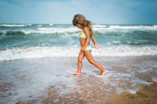 Bambina allegra gode di una giornata in spiaggia mentre ci si rilassa in mare in una soleggiata giornata estiva calda. Vacanze estive e concetto di relax