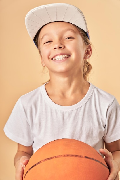 Bambina allegra in berretto che tiene la palla da basket