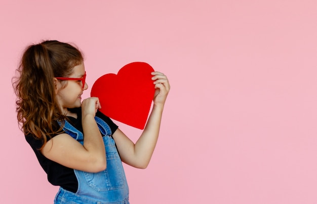 Bambina allegra in occhiali rossi che tengono a forma di cuore