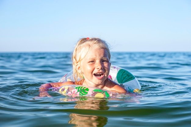 Bambina allegra nuota nel mare con un anello gonfiabile