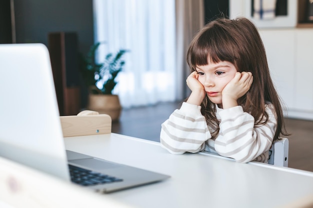 Bambina annoiata che guarda un computer portatile