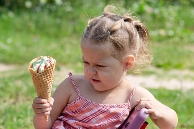 Bambina arrabbiata che guarda il corno di gelato della cialda con sconcerto nel parco estivo