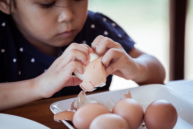 Bambina asiatica che aiuta madre a sbucciare un uovo