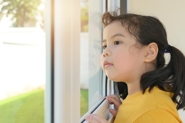 Bambina asiatica che guarda fuori dalla finestra Resta a casa in quarantena Bambina che vuole uscire