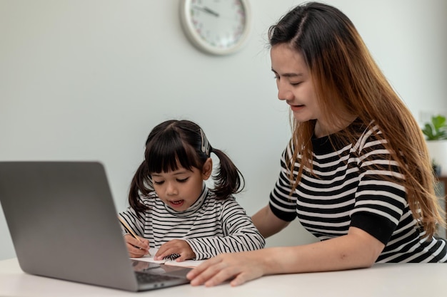 Bambina asiatica che impara la lezione online a casa con la madre Il bambino in età prescolare usa il computer portatile per fare i compiti a casa dall'insegnante di scuola tramite internet digitale remoto con il supporto della mamma