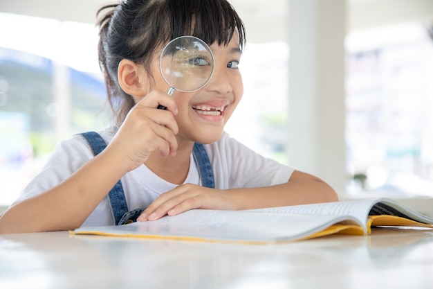 Bambina asiatica che legge i libri sulla scrivania con una lente d'ingrandimento