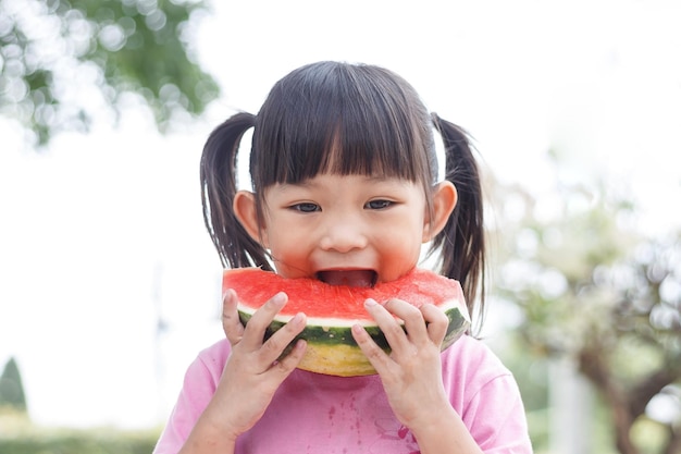 Bambina asiatica che mangia e morde un pezzo di anguria