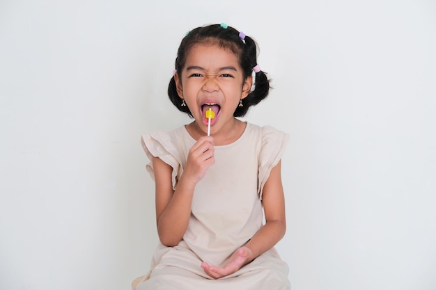 Bambina asiatica che mostra un'espressione buffa del viso mentre mangia caramelle lecca-lecca