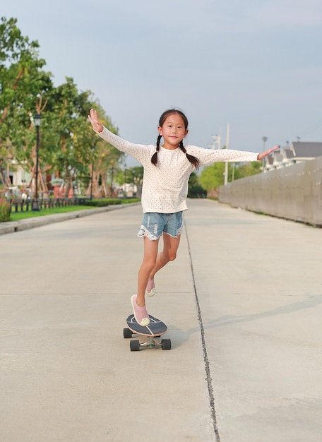 Bambina asiatica che pattina su uno skateboard Bambino che cavalca sullo skateboard all'aperto in strada Lei skateboard sulla strada