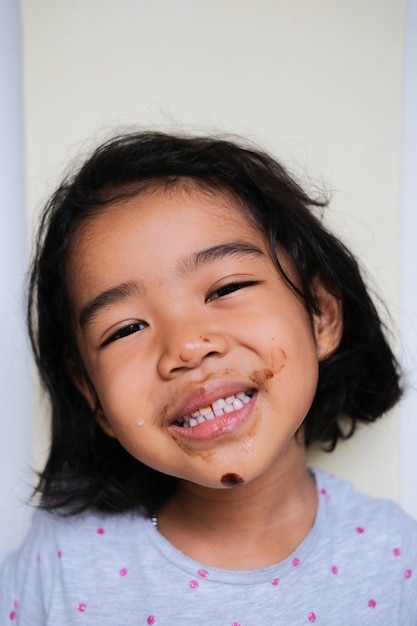 Bambina asiatica che sorride felice dopo aver mangiato il gelato con la bocca sporca