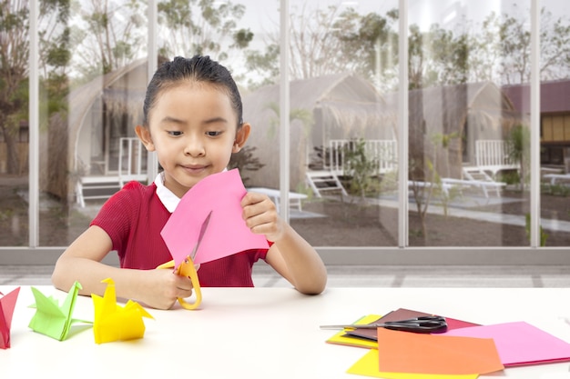 Bambina asiatica che taglia una carta a casa