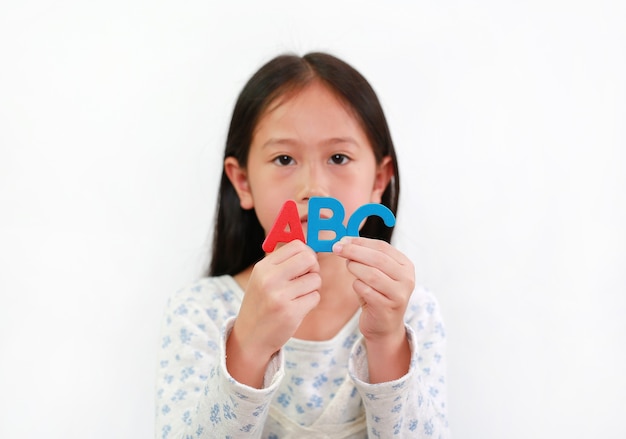 Bambina asiatica che tiene il testo della spugna ABC nelle mani su sfondo bianco. Concentrati sulle lettere in mano
