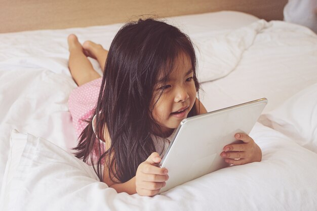 Bambina asiatica che utilizza il computer della compressa a letto