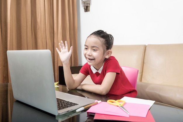 Bambina asiatica con laptop che frequenta la lezione di scuola online a casa. Educazione online durante la quarantena