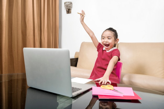 Bambina asiatica con laptop che frequenta la lezione di scuola online a casa. Educazione online durante la quarantena