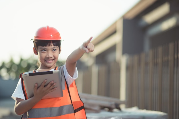 Bambina asiatica con un casco di sicurezza in testa e un tablet in mano in un cantiere edile